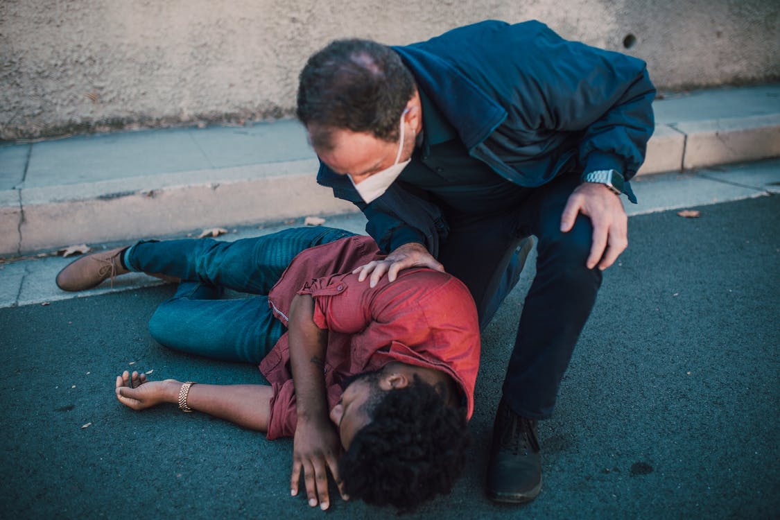 A paramedic in a face mask checks on a man lying in the street.
