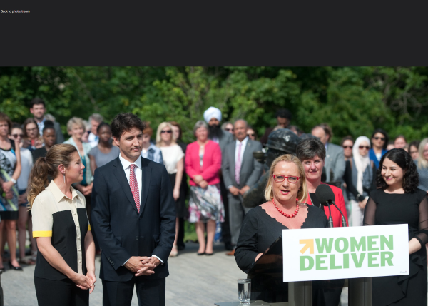 Justin Trudeau stands in support of woman giving speach at podium for Women Deliver event.